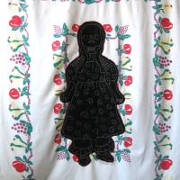 From the series American Memento Mori: Doll - applique and embroidery on vintage textile. A folk art doll silhouette with a skeleton head is appliquéd onto a colorful vintage tablecloth, and embellished with white embroidery.